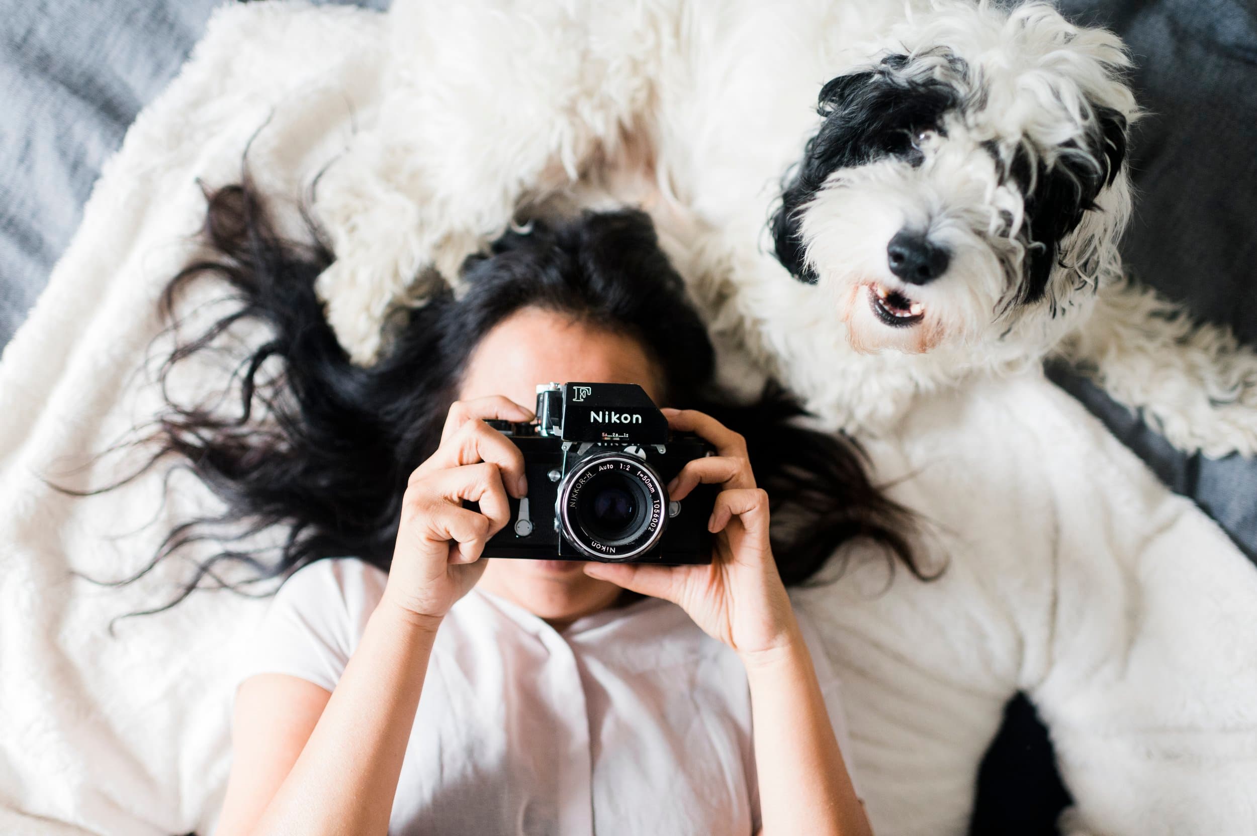 Razia Jukes holding a vintage camera, lying beside her dog
