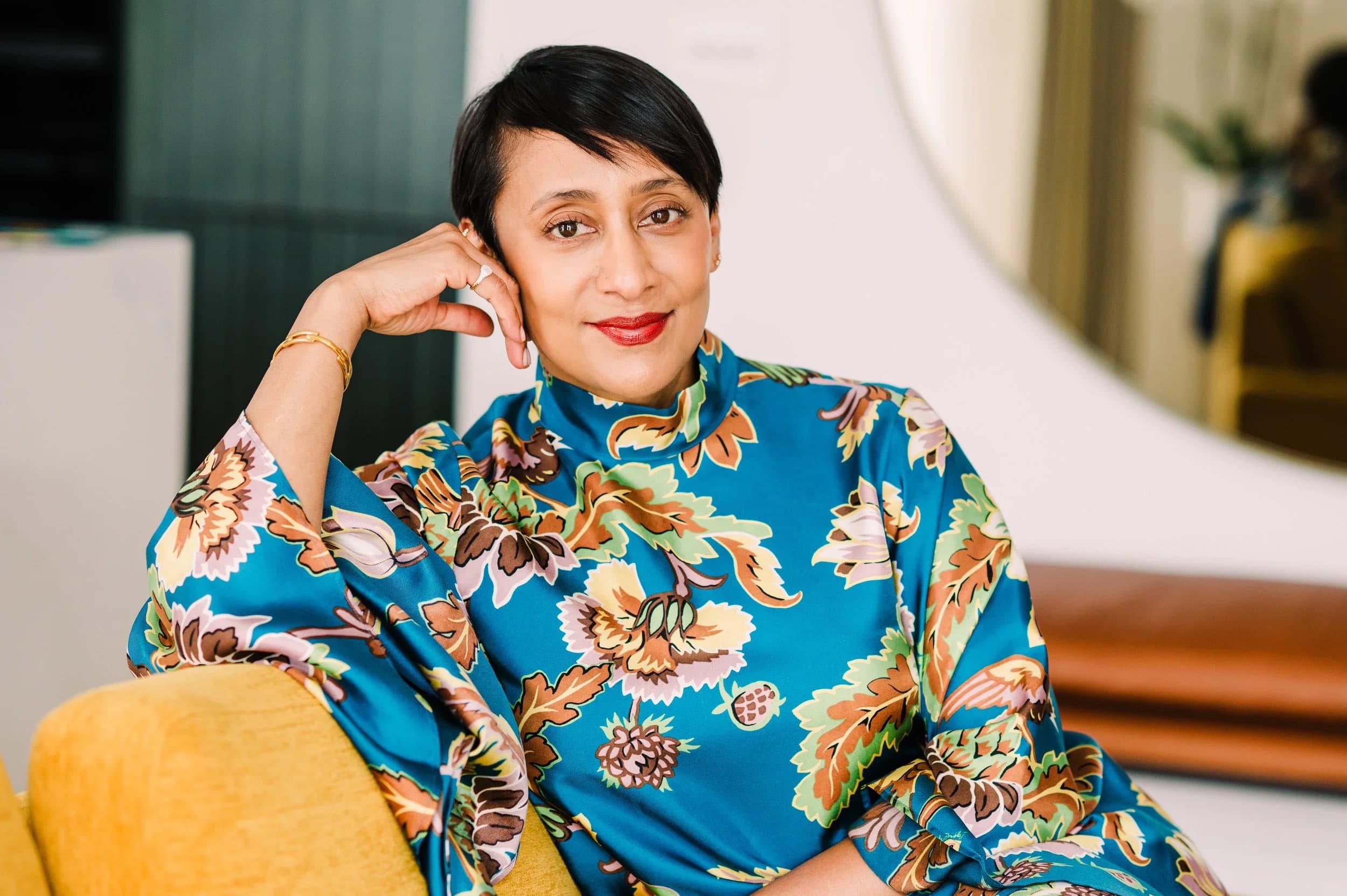 A woman in a blue floral blouse resting her head on her hand on a yellow sofa