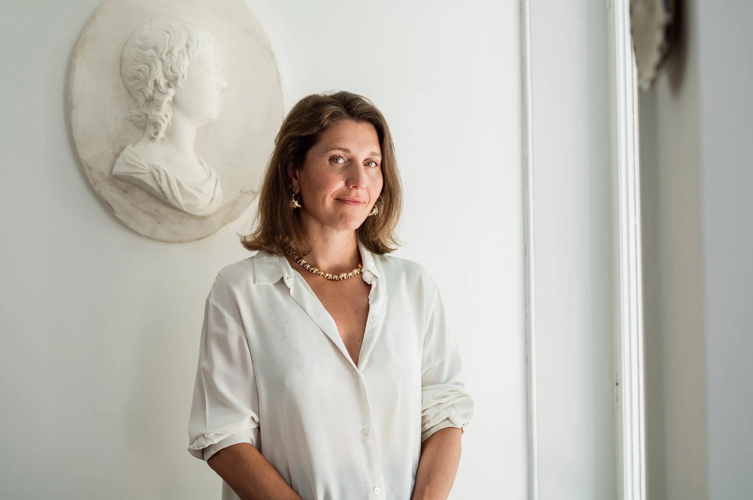 A woman in a white shirt standing beside a plaster relief