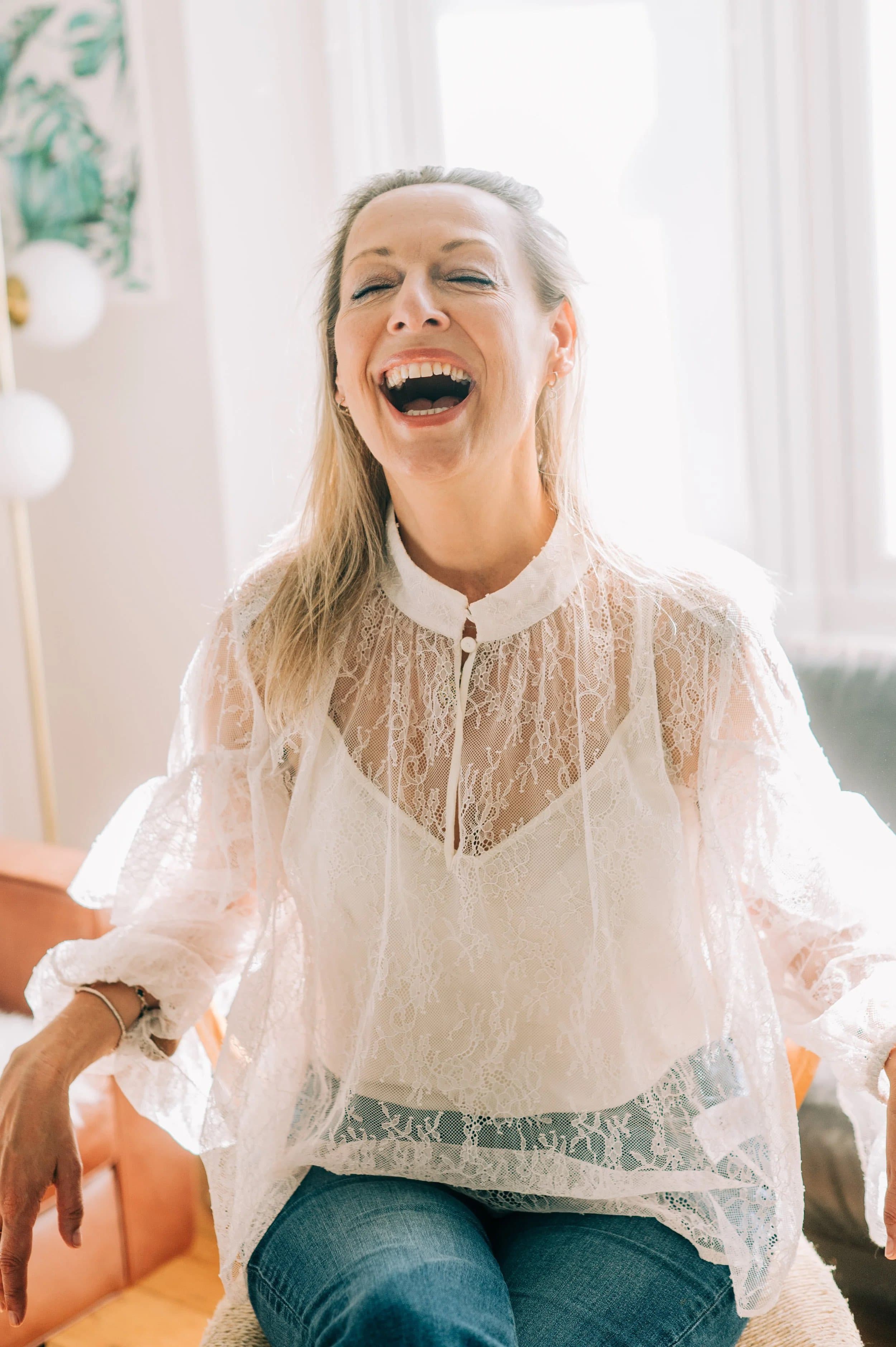 A woman in a white lace blouse laughing with her head thrown back