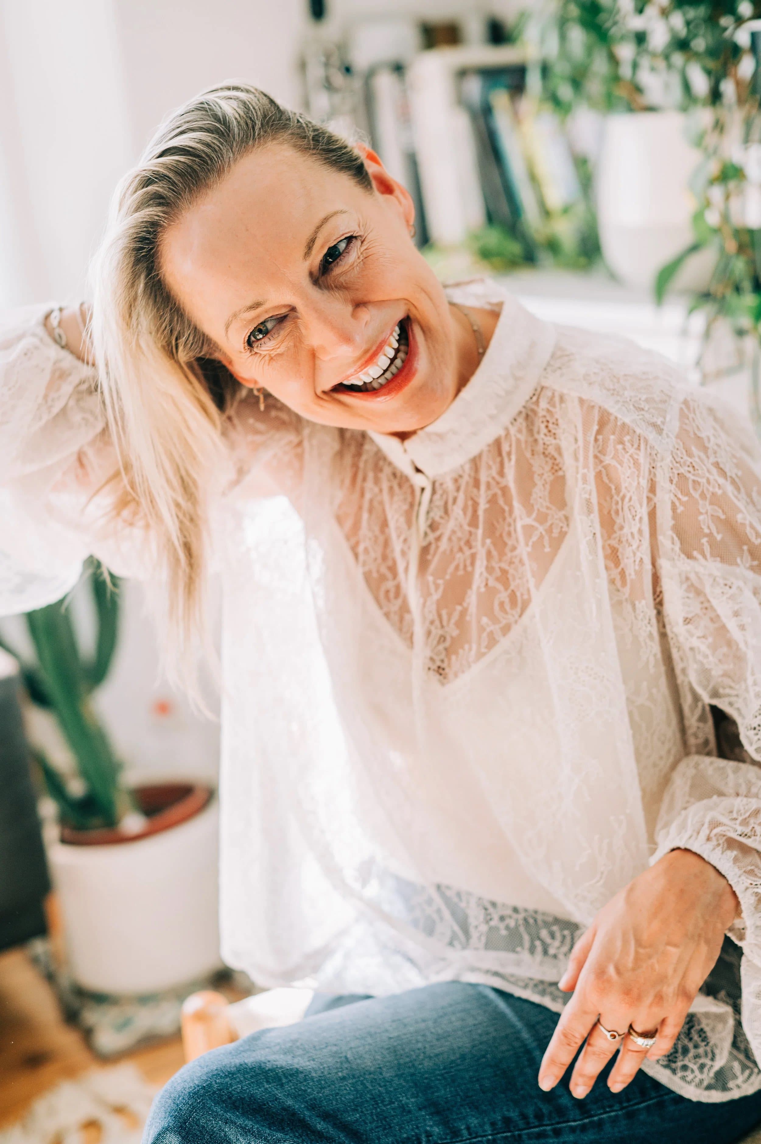 A laughing woman in a white lace blouse leaning towards the camera