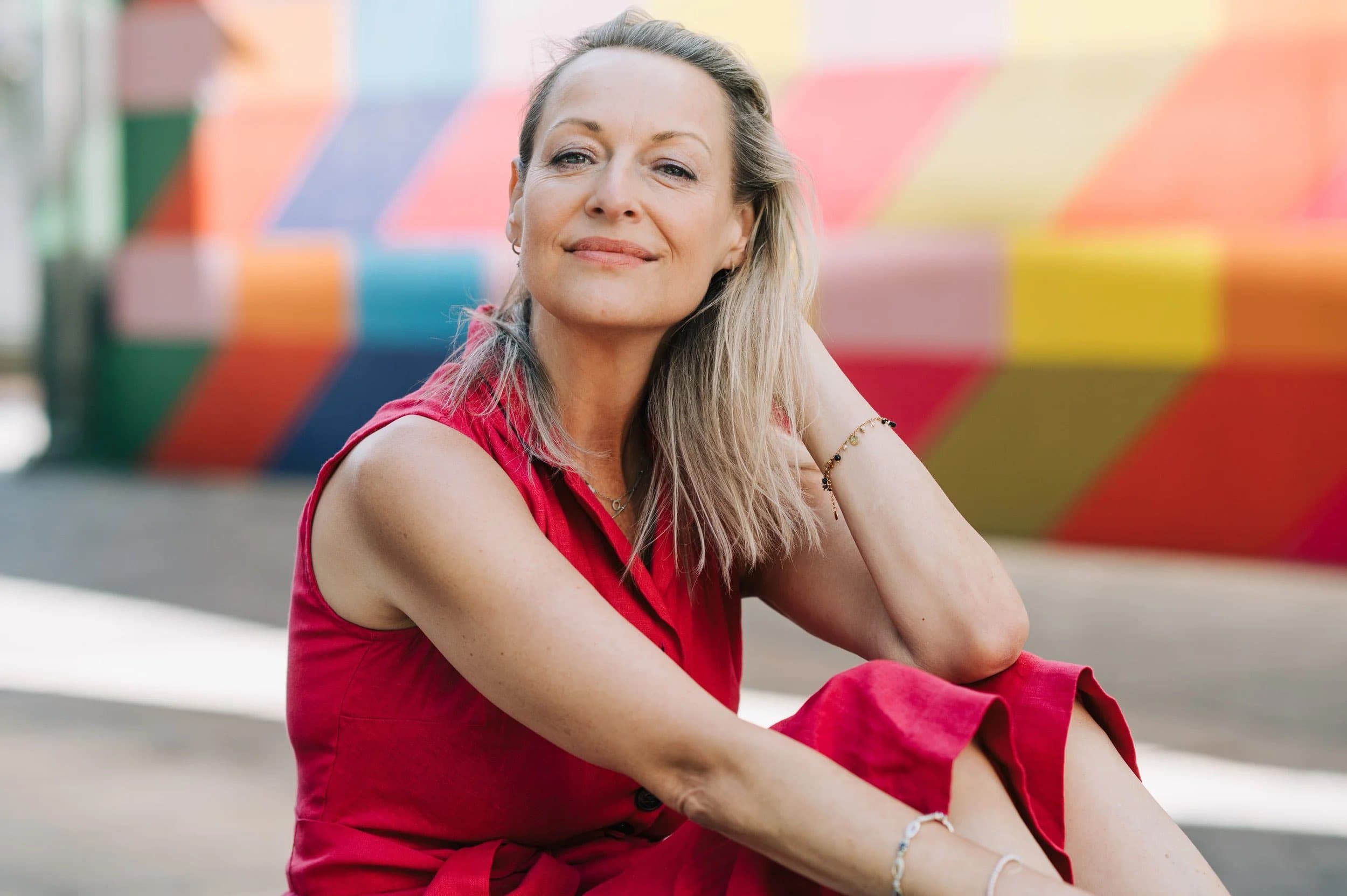 A woman in a red sleeveless dress seated in front of a brightly painted wall