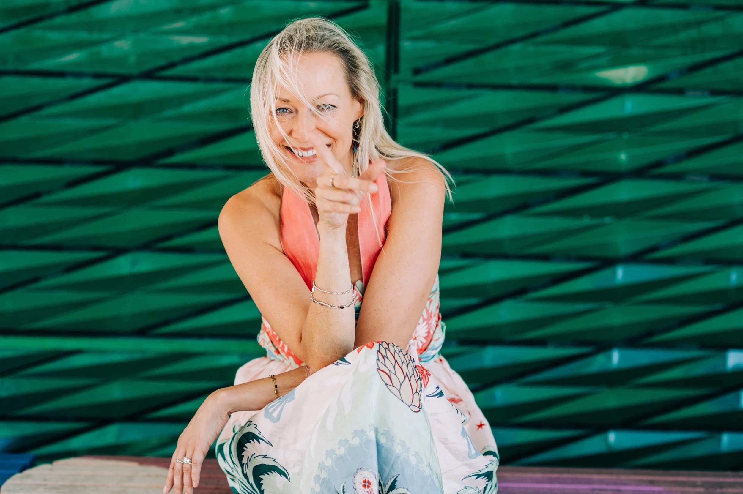 A smiling woman in a coral top seated in front of a green tiled wall