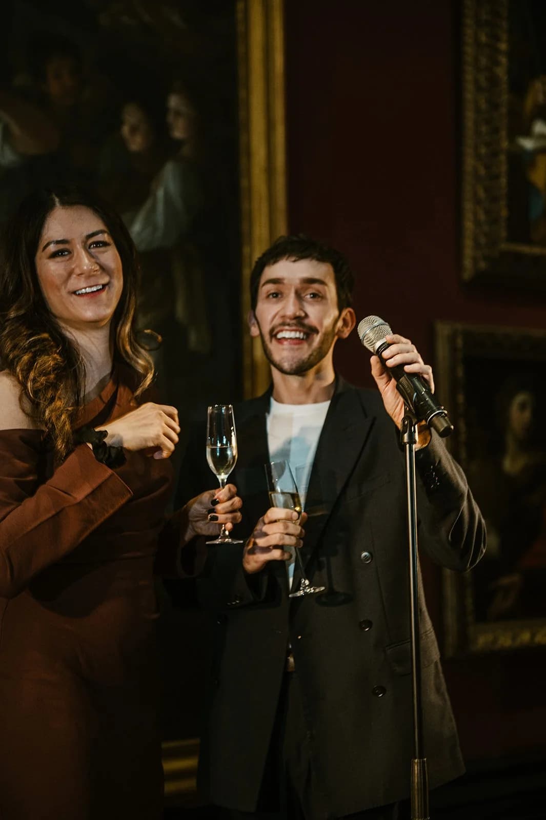 A man singing into a microphone beside a smiling woman holding champagne