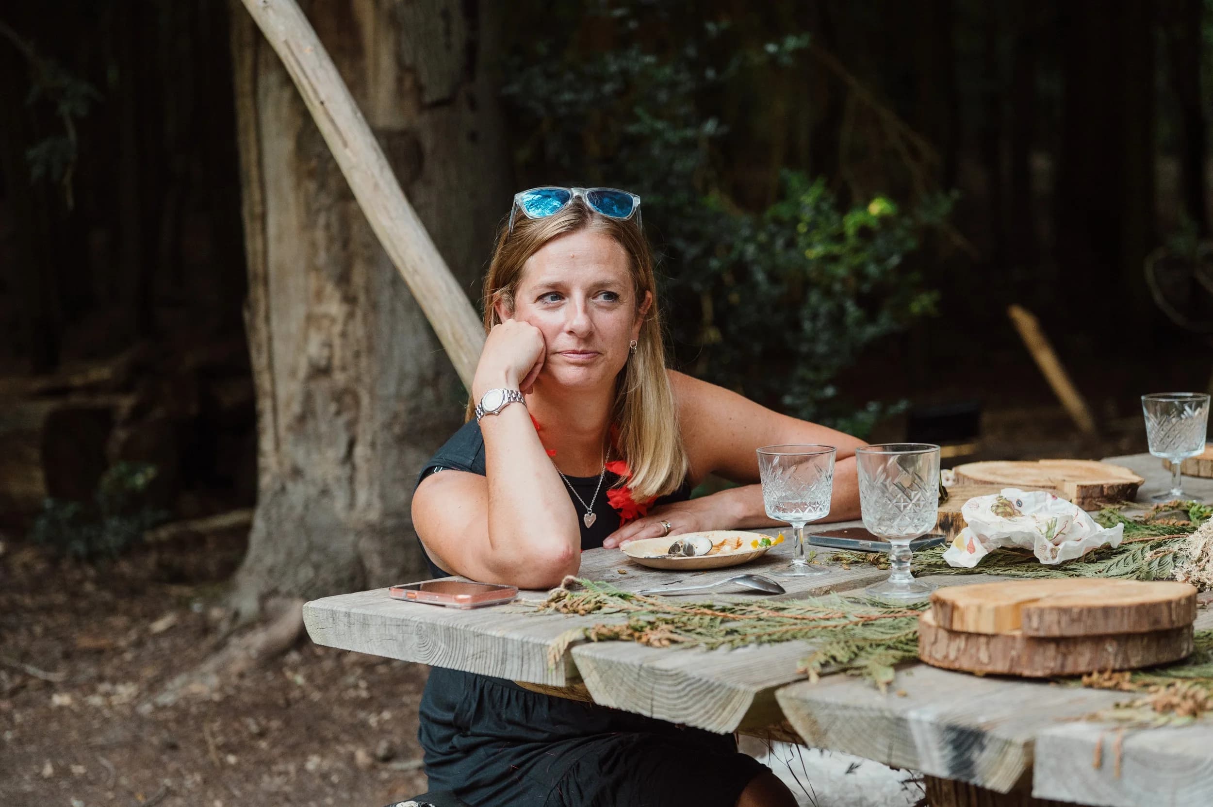 A woman with sunglasses on her head resting her chin on her hand at a rustic outdoor table