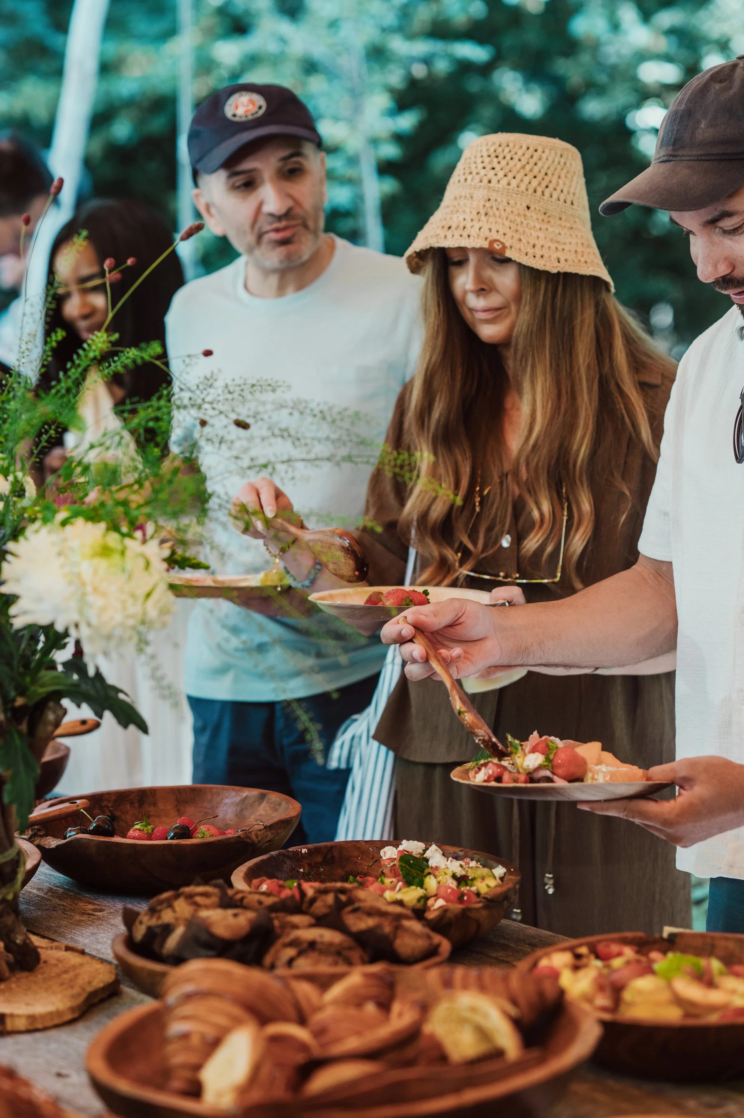Guests helping themselves from wooden bowls of salads and bread at an outdoor buffet