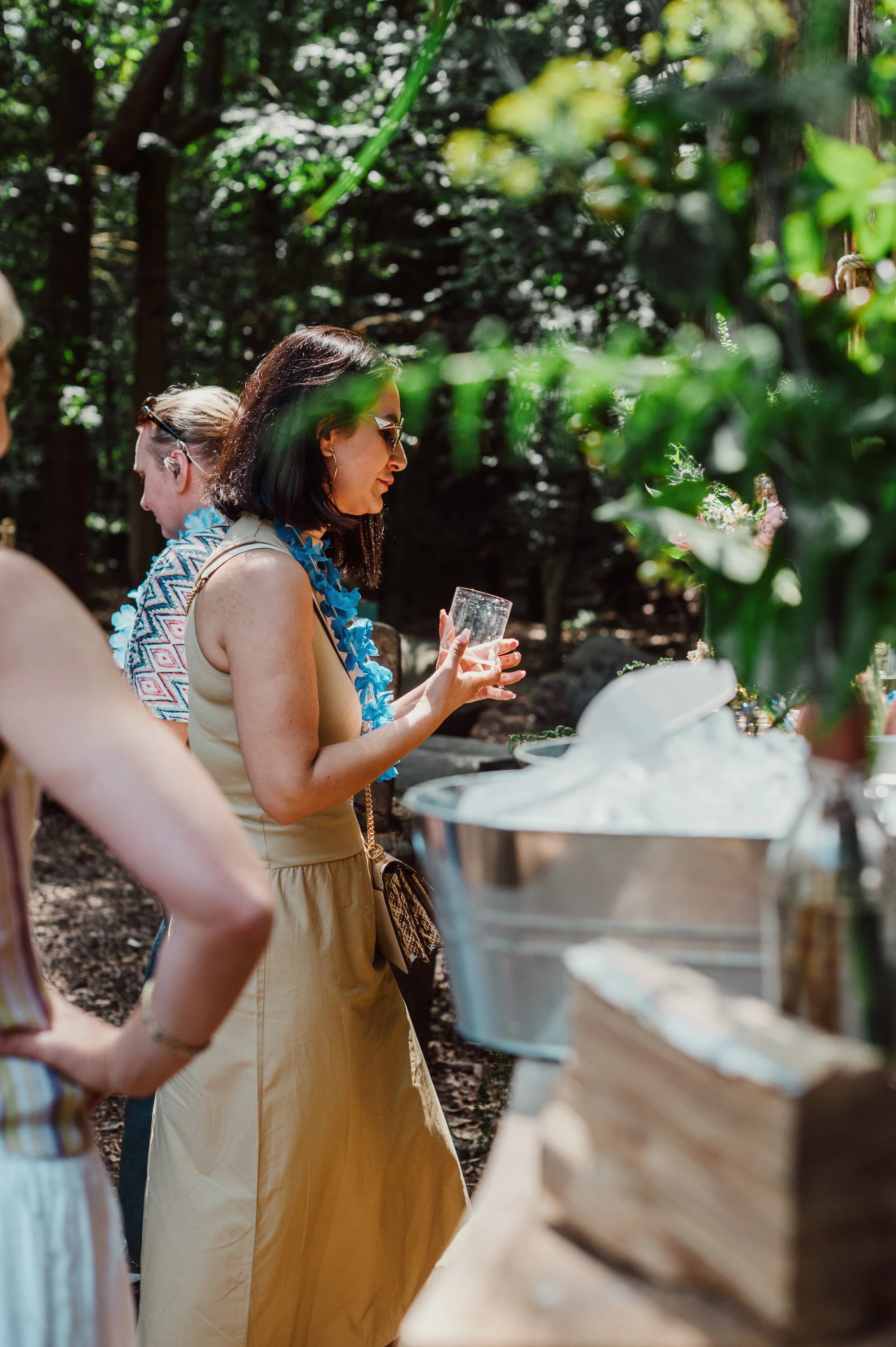 A woman in a blue garland and long beige dress holding a glass beside an ice bucket