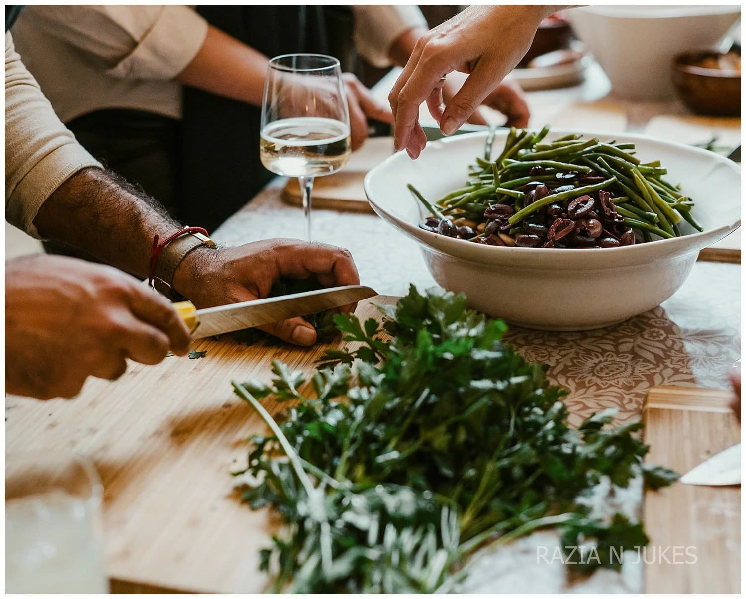 Hands chopping herbs beside a bowl of green beans and a glass of wine