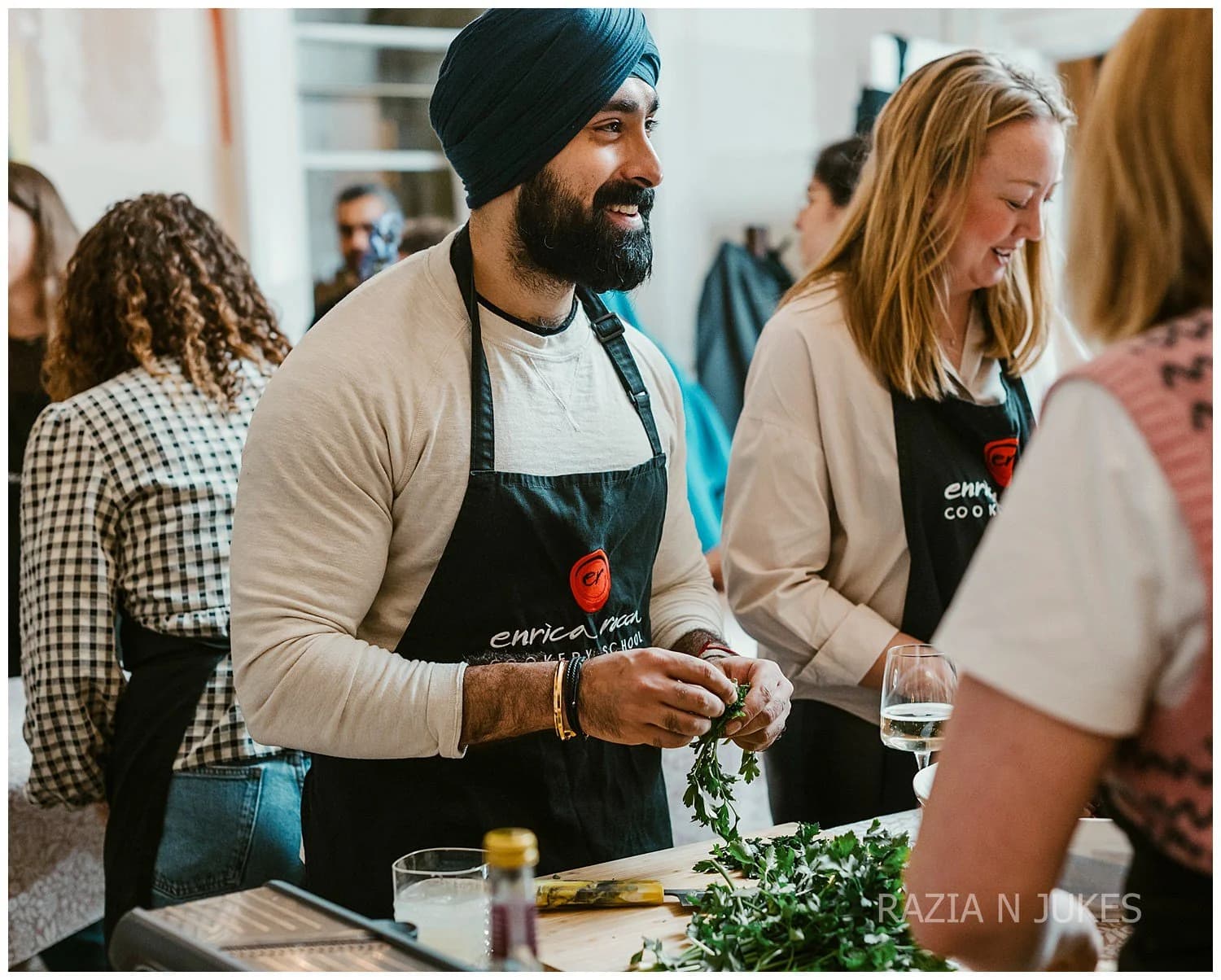 A chef in a turban and apron picking herbs with guests at a cookery event