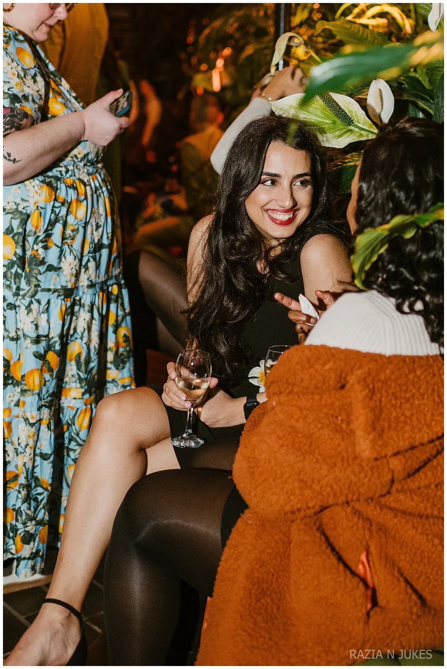 A woman in a black dress laughing with friends on a leather sofa