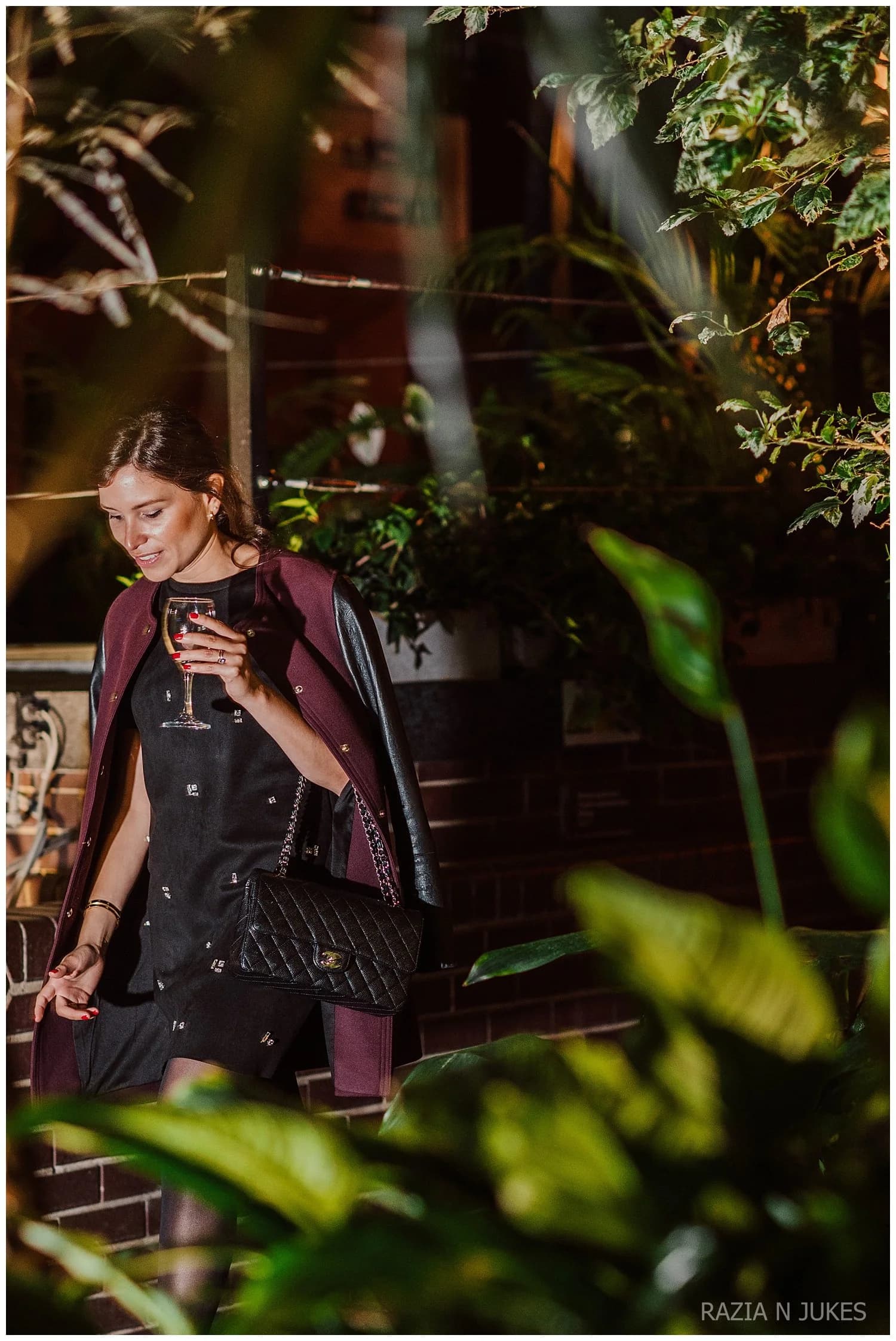 A guest holding a glass of wine, seen through foliage
