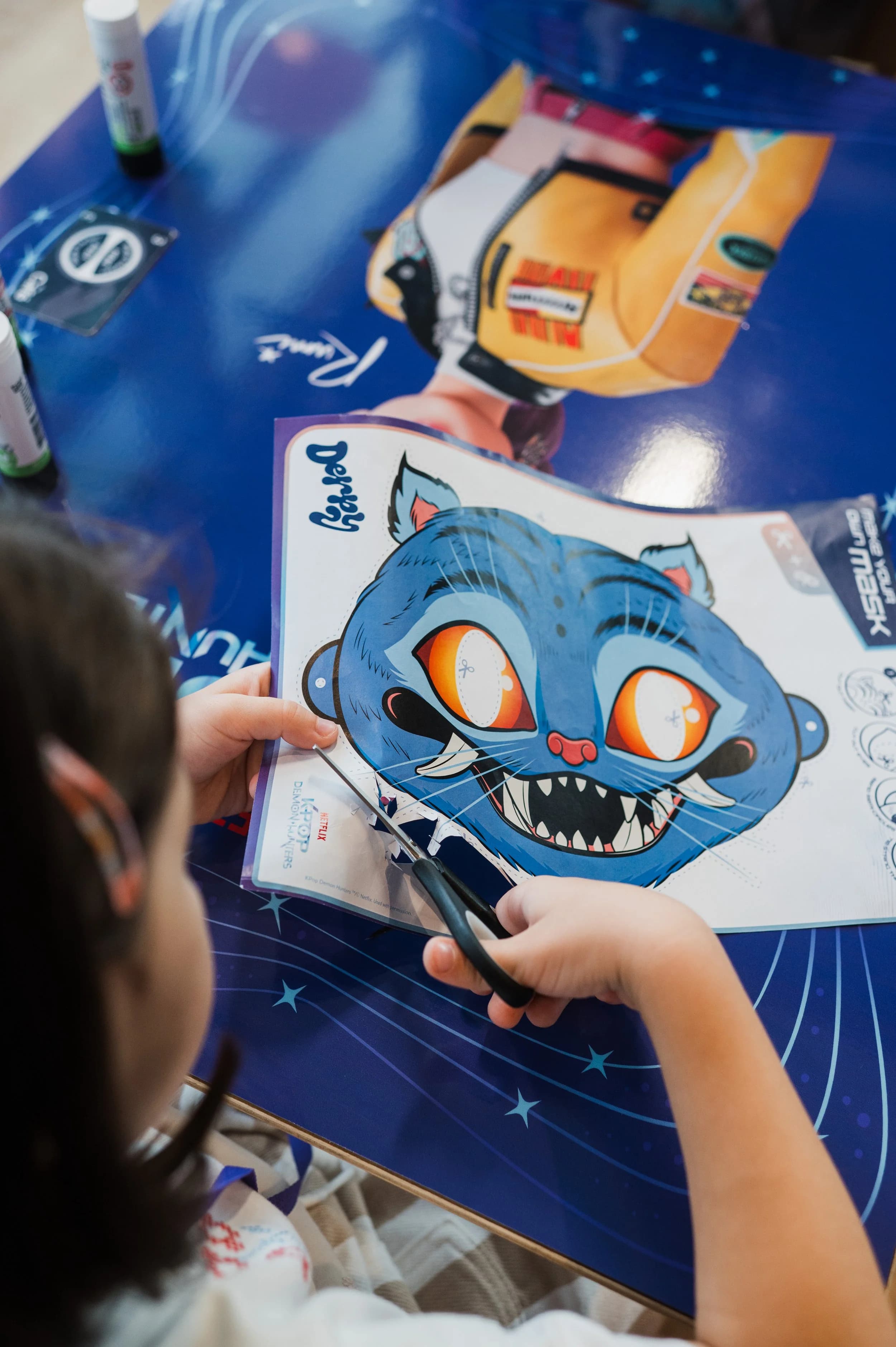 A child cutting out a blue cartoon cat mask from a printed sheet at a table