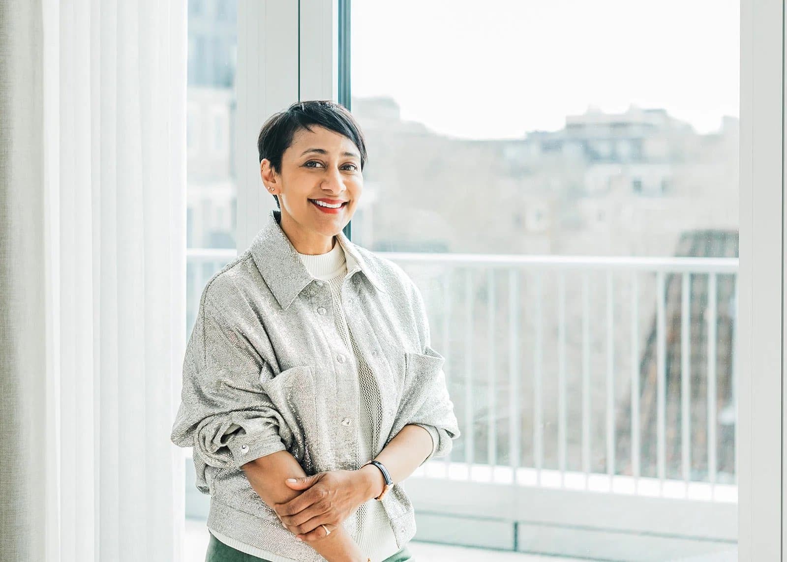 A woman with short dark hair in a grey shirt standing by a balcony window