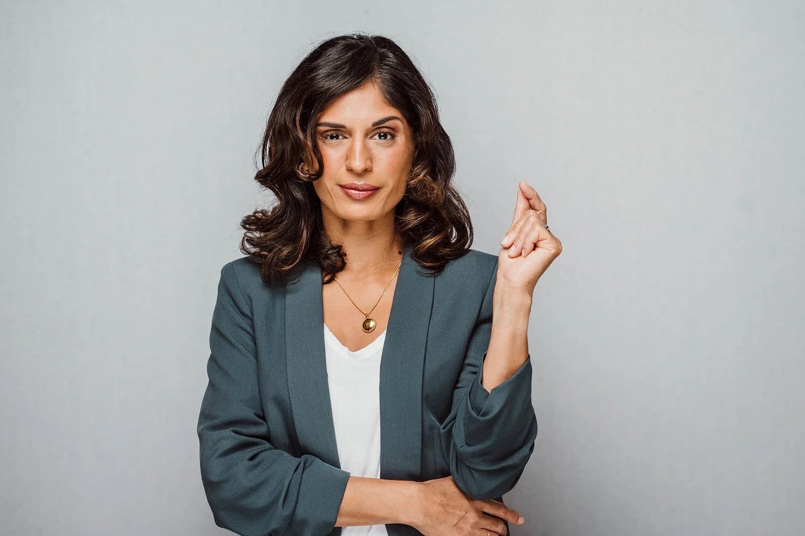 A woman in a teal blazer with one hand raised, against a pale backdrop