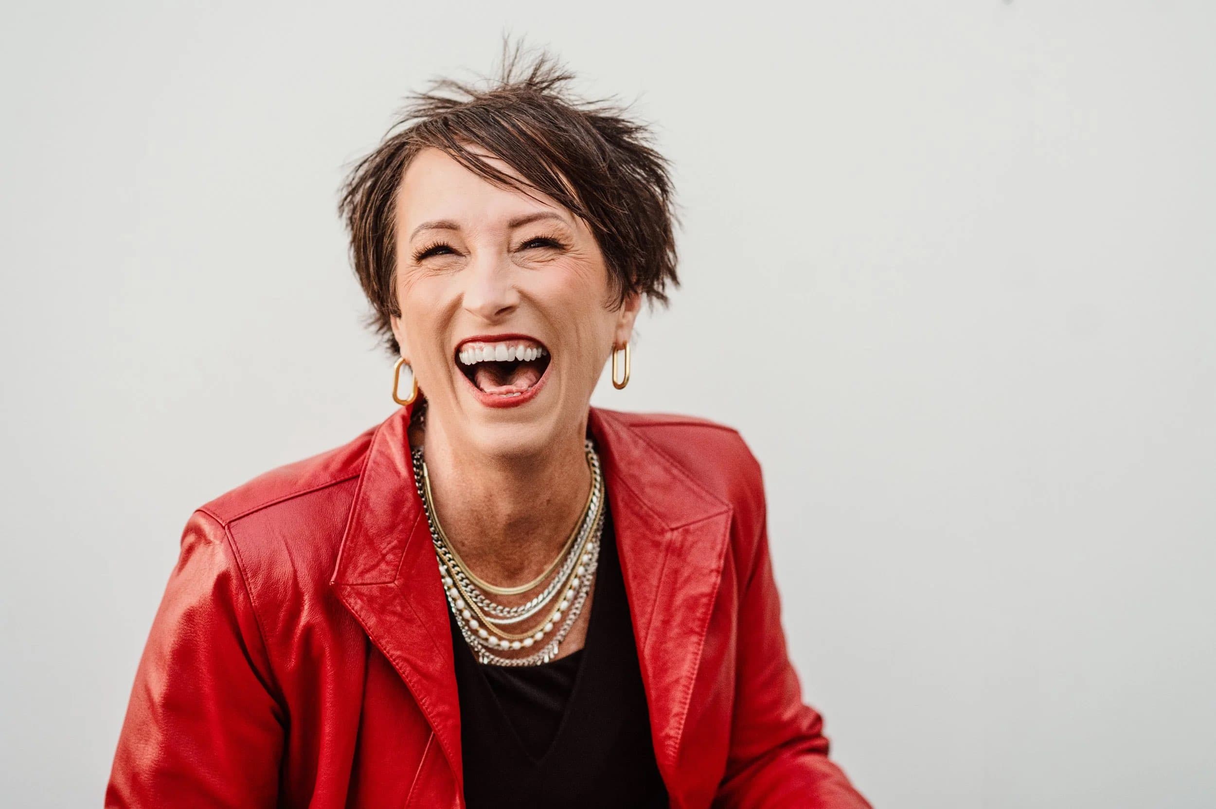 A laughing woman with short hair in a red leather jacket