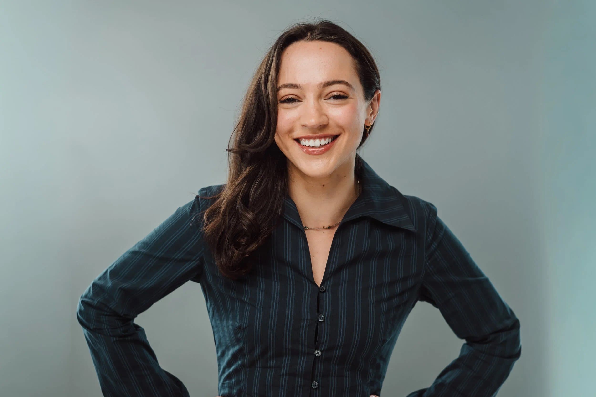A smiling woman in a dark striped shirt with hands on hips